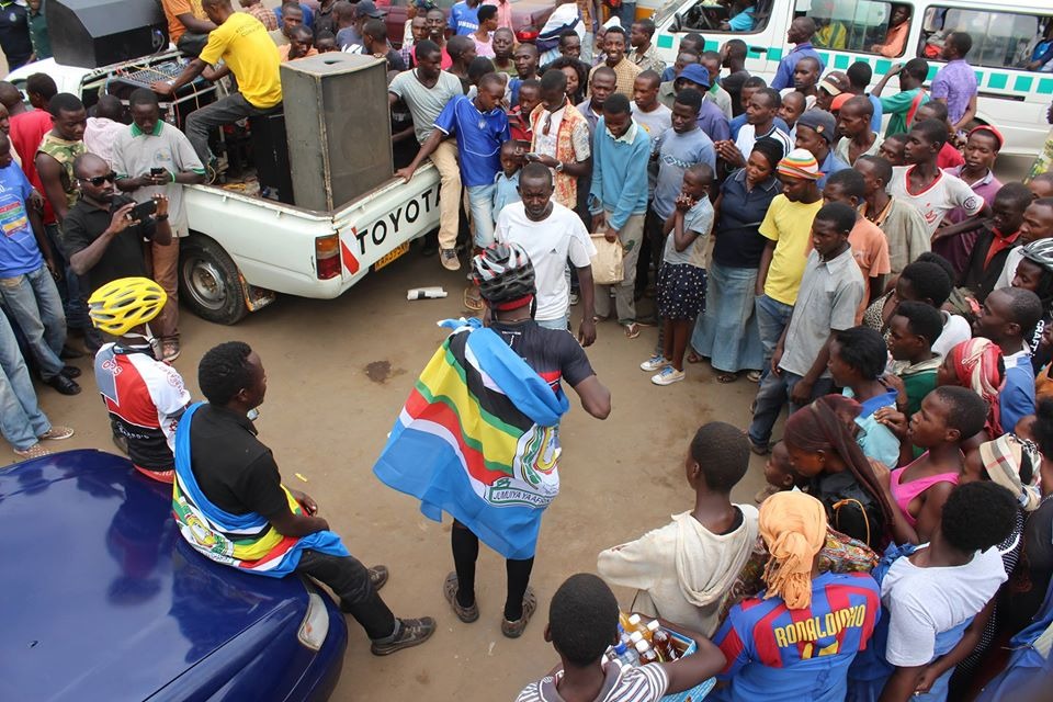 Crowd gathered around a cyclist draped in the East African Community flag