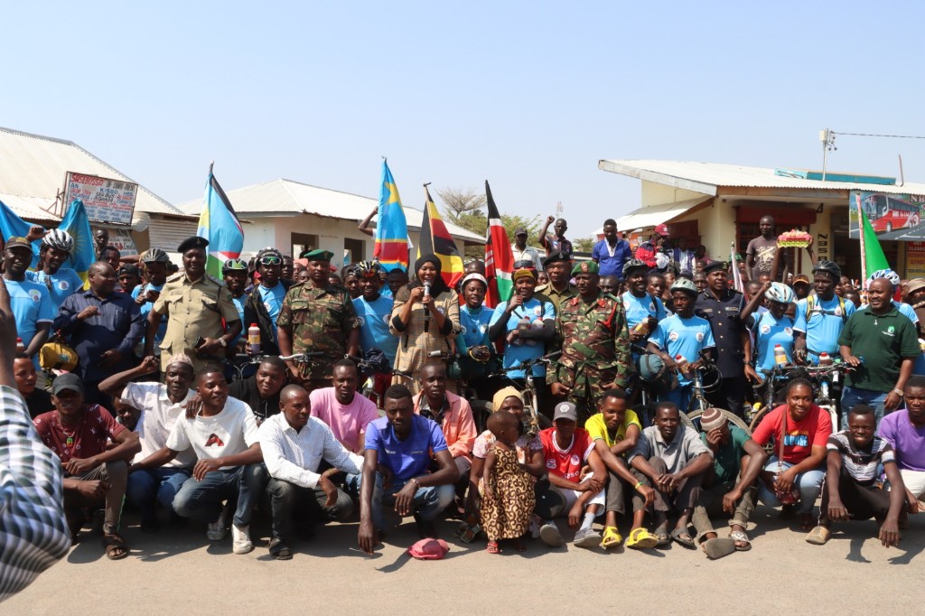 Large community gathering with cyclists, officials, and national flags welcoming the expedition