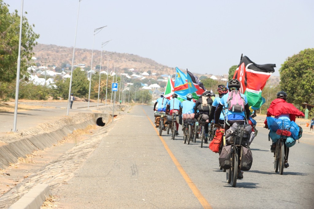 Cyclists riding with Kenyan, Congolese, and South Sudanese flags on the expedition route