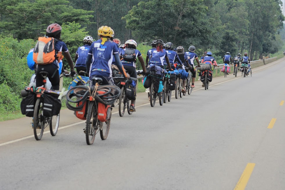 Long line of GACS cyclists riding in formation on a paved road through hills